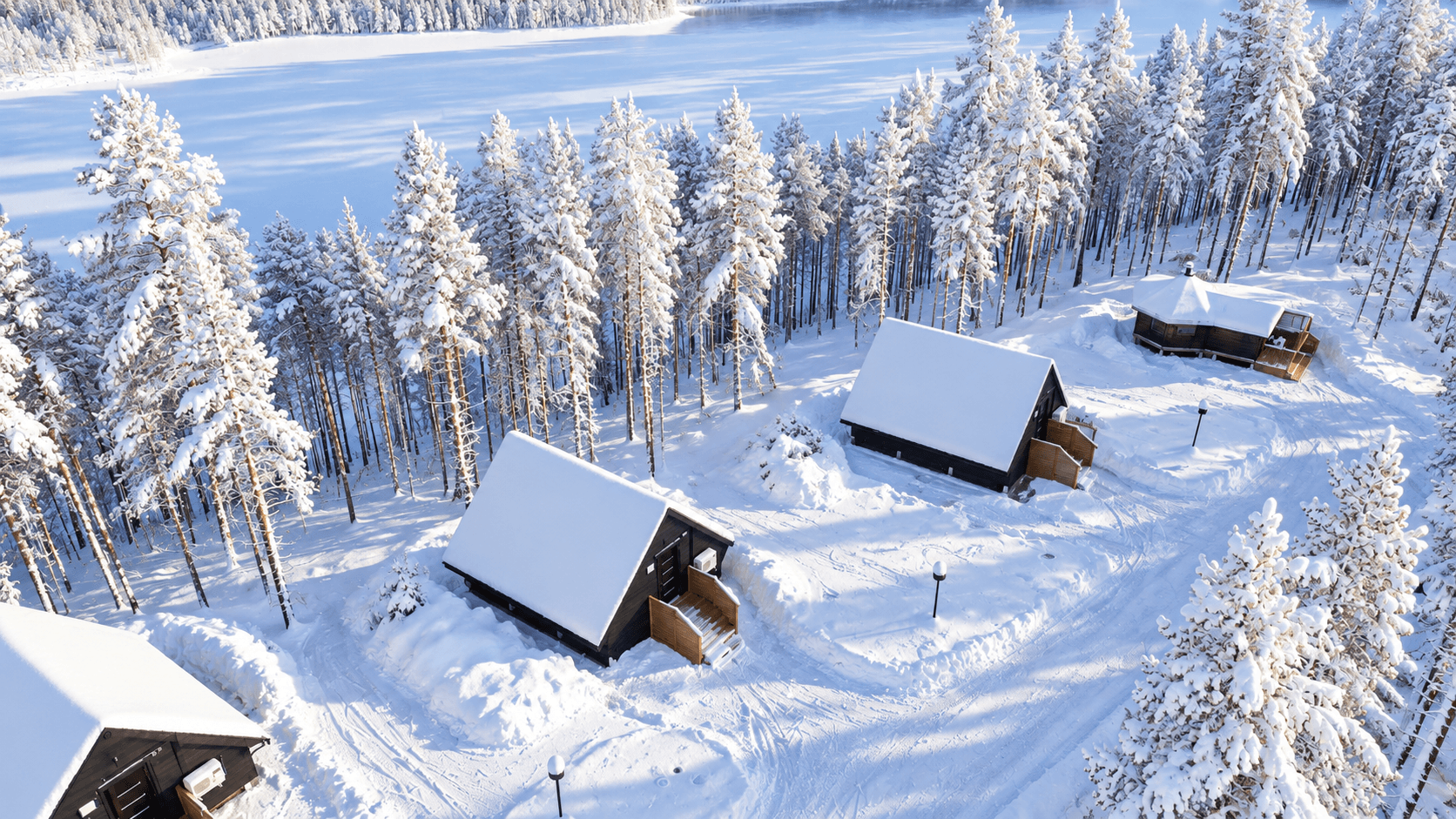 Verschneite Hütten des Hera Resort im winterlichen Kiefernwald am See